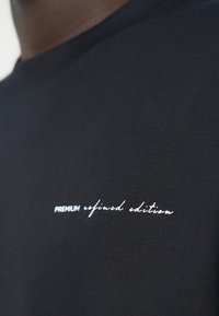 Μαύρο βαμβακερό μπλουζάκι με στρογγυλή λαιμόκοψη. Κείμενο "PREMIUM refined edition" σε λευκή καλλιτεχνική και έντονη γραμματοσειρά στο στήθος. Ομαλή υφή.