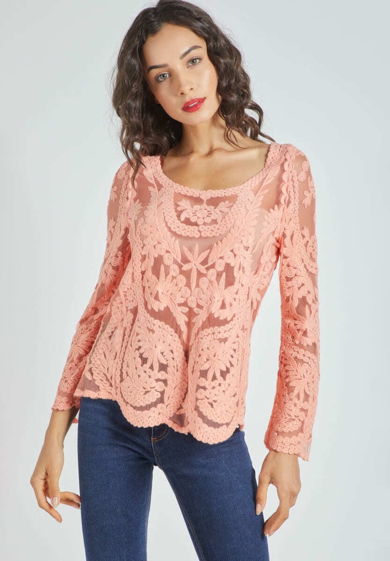 Top de encaje durazno con mangas largas, adornado con bordados florales, un cuello redondeado y un dobladillo con forma de pico, superpuesto sobre una base sólida.