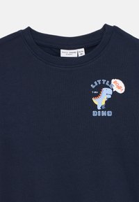 Merenneitomainen pitkähihainen collegepusero, jossa on pyöreä kaula-aukko. Puserossa on leikkisä T-rex -kuvio ja teksti "LITTLE DINO" vaaleansinisellä ja valkoisella.