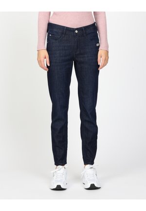 Dunkelblaue Denim-Jeans mit schlankem Schnitt, ausgestattet mit Fronttaschen und einem Knopfverschluss. Dazu weiße Sneaker und ein rosa geripptes Sweater.