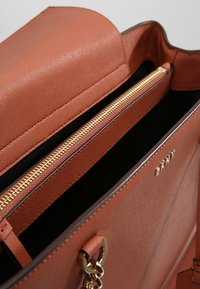 Sac à main en simili cuir marron avec une finition texturée, fermeture éclair dorée, et intérieur noir. Dispose d'une bandoulière et de compartiments zippés.