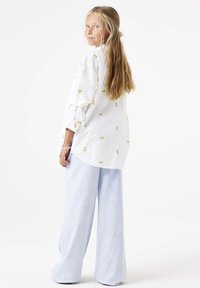 Camisa blanca de botones con un patrón de frutas en verde y amarillo, combinada con pantalones de mezclilla anchos de lavado claro. Tela suave, corte relajado.