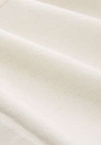 Tejido color beige claro con finas rayas verticales, que presenta una textura suave y un sutil brillo, plegado para mostrar capas y contornos.
