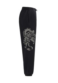 Svarta sweatpants med elastisk midja har en stor grå drakegrafik på vänster ben. Taperad passform med muddar vid anklarna.