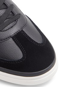 Zapatilla de cuero negro y ante con punta redondeada, acentos texturizados, detalles de costura y suela de goma blanca.