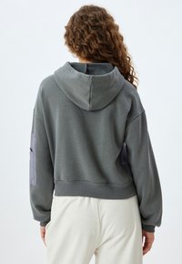 Sudadera con capucha gris de diseño corto y acentos de tela en contraste en las mangas. Textura suave, dobladillo acanalado y corte relajado.