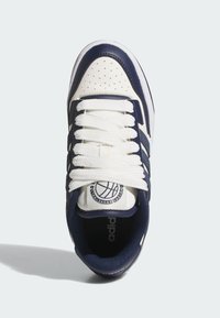 Biele a námornícke športové tenisky s perforovanou kožou, rovnými bielymi šnúrkami a okrúhlym logom na jazyku. Textúrovaná tkanina na bokoch.