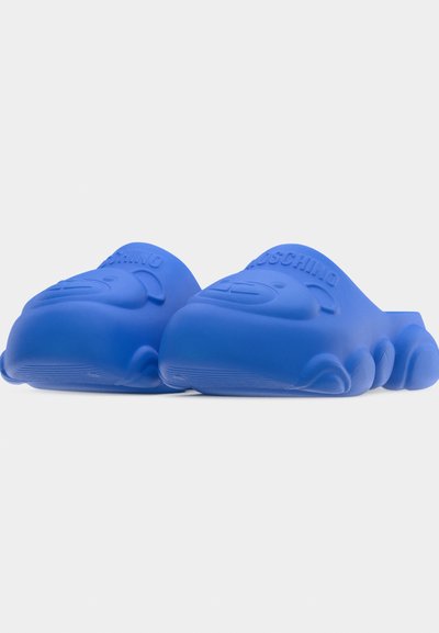 Ζευγάρι μπλε slides Moschino με ανάγλυφα πρόσωπα αρκουδάκια και λογότυπο στα λουράκια, εμφανιζόμενα σε απλό λευκό φόντο.