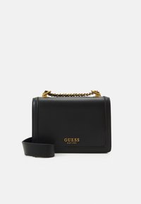 Zwarte leren handtas met een gestructureerd ontwerp, gouden ketting en hardwareaccenten, en een afneembare schouderriem. "GUESS EST1981" logo in goud.