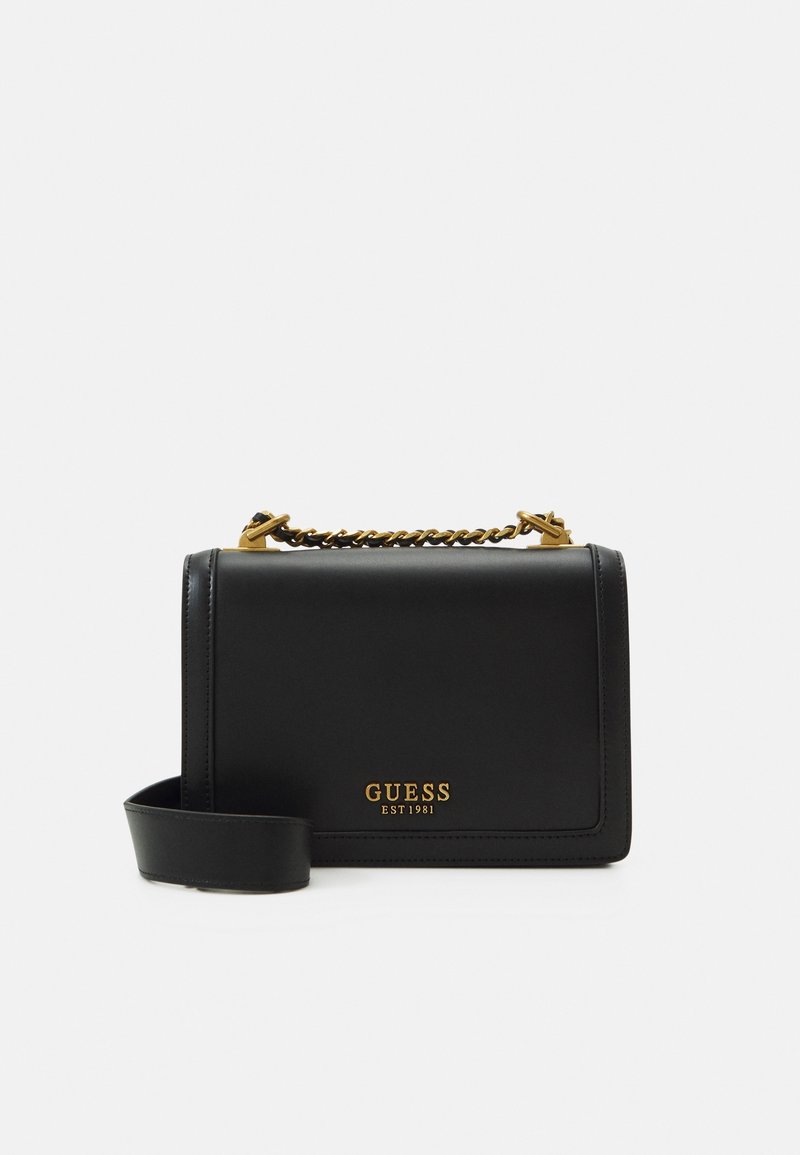 Zwarte leren handtas met een gestructureerd ontwerp, gouden ketting en hardwareaccenten, en een afneembare schouderriem. "GUESS EST1981" logo in goud.