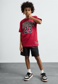 Červené bavlnené tričko s grafickým motívom "JORDAN 23" v čiernej farbe, v kombinácii s čiernymi šortkami a čiernymi teniskami s bielymi akcentmi.