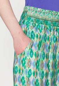 Calças com padrão verde e azul, possuem um cós elástico, um bolso lateral e são feitas de um tecido leve e texturizado.