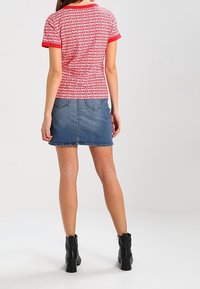 Camisa de manga corta a rayas rojas y blancas con un cuello rojo sólido, combinada con una falda de mezclilla azul y botas de tacón negro a la altura del tobillo.