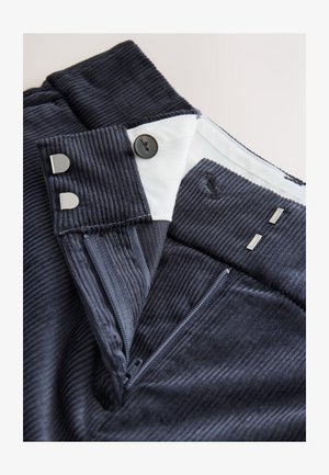 Navy corduroy trousers featuring a front zipper, button closure, and silver-tone hardware. The fabric has a textured ribbed pattern.