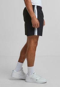 Shorts noirs avec des rayures blanches sur les côtés, taille élastique et coupe décontractée, associés à des baskets blanches et des chaussettes blanches.