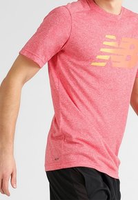Red heathered T-shirt with short sleeves, featuring a large yellow logo and horizontal stripes. Made of a lightweight, breathable material.