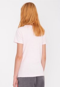 Vaaleanpunainen puuvillainen T-paita, jossa on lyhyet hihat ja pyöreä kaula-aukko. Paidalla on sileä pinta ja löysä istuvuus. Yksinkertainen muotoilu ilman näkyviä kuvioita.