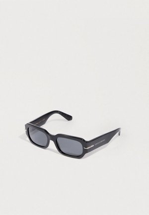 Occhiali da sole rettangolari neri con lenti scure, montatura in plastica spessa, dettagli in argento sulle tempie e marchio su un lato.