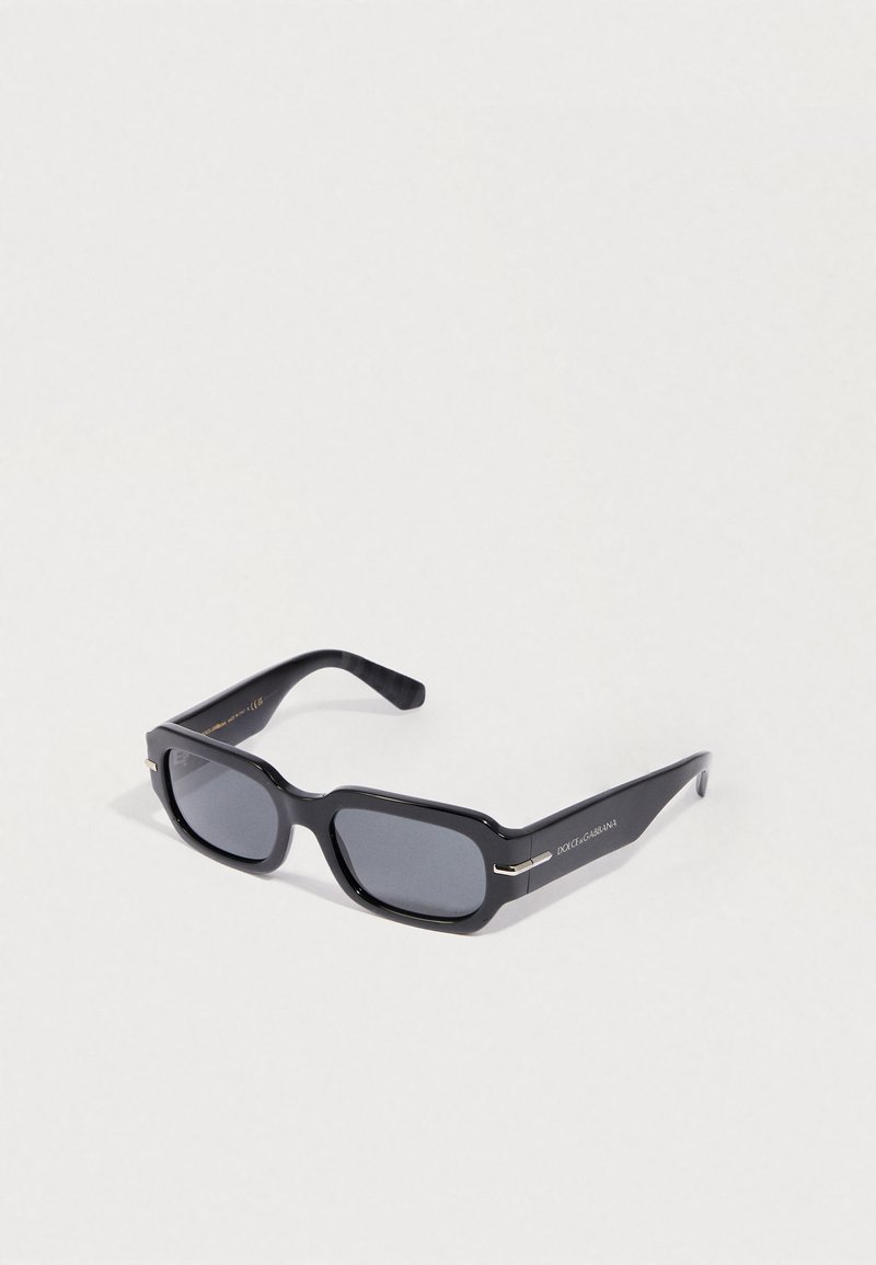 Fekete téglalap alakú napszemüveg sötét lencsékkel, vastag műanyag kerettel, ezüst díszítéssel a szárakon, és logóval az egyik oldalon.