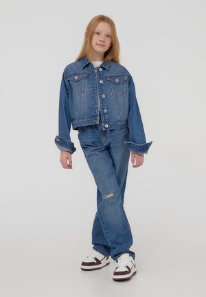 Giubbotto di jeans tagliato con chiusura a bottoni e due tasche sul petto, abbinato a jeans a vita alta di colore chiaro con dettagli strappati.