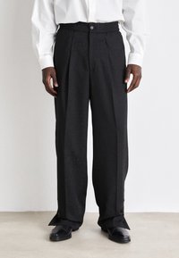 Black, wide-legged trousers with a textured pattern, elastic waistband, and button closure, featuring side slits at the hem.