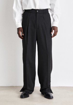 Black, wide-legged trousers with a textured pattern, elastic waistband, and button closure, featuring side slits at the hem.