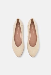 Ett par balettklipp i beige vävt tyg med rundade tår och vadderade innersulor, sedd ovanifrån på en vit bakgrund.