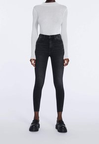 Jeans skinny negros de cintura alta con una textura suave, combinados con una camiseta de manga larga blanca con canalé. El conjunto incluye zapatos negros de suela gruesa.