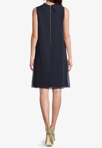 Navy sleeveless dress with a subtle collar, back zipper, and sheer overlay. Paired with beige high-heeled shoes.