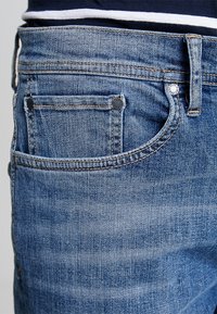 Ljusblå denimjeans med en slät textur, med en bakficka, sydda sömmar och metallnitar för förstärkning.