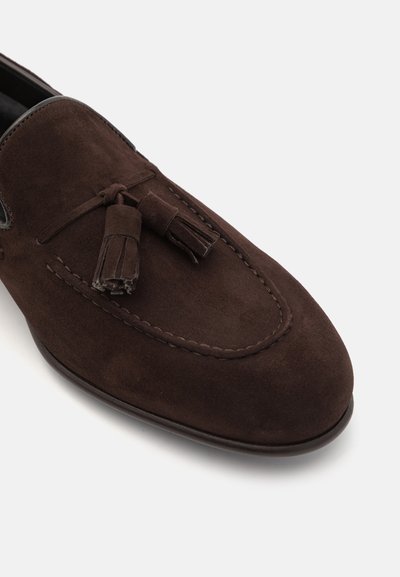 Brown suede loafers with a stitched design, featuring tassel accents and a smooth sole. Textured surface with a rounded toe.