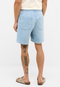 Shorts de mezclilla azul claro con cinturilla elástica, que cuentan con dos bolsillos traseros y un corte holgado. Textura suave, diseño a la altura de la rodilla.