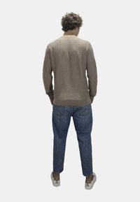 Maglione beige a maniche lunghe con un motivo testurizzato, abbinato a jeans in denim blu. Il modello indossa scarpe da ginnastica grigie. Vista da dietro.