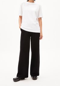 Vit bomullströja med rund hals, kombinerad med lösa svarta byxor. Skorna är svarta träskor med metallnitar.