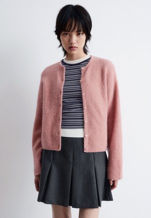 Light pink, fuzzy cardigan with a round neck and button closure, worn over a striped shirt. Gray pleated skirt completes the outfit.