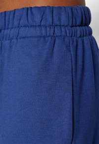 Μπλε joggers με ελαστική μέση από μαλακό, υφασμάτινο υλικό. Περιλαμβάνει συμποσμένη μέση και πλευρικές τσέπες.