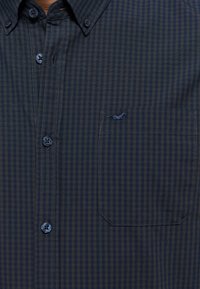 Camicia a maniche lunghe a quadri blu e marrone con colletto a punte, taschino sul petto e ricamo del logo discreto. Tessuto in misto cotone.
