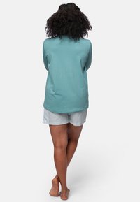 Helles blaues Langarmoberteil, kombiniert mit gestreiften Shorts. Der Stoff scheint weich zu sein, mit einem lässigen Design und einer subtilen Textur.