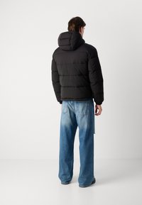 Giubbotto imbottito nero con cappuccio, design a righe orizzontali e polsini a coste, abbinato a jeans blu larghi con finitura scolorita.