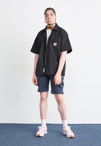 Svart kortermet skjorte med logo, grå cargo shorts og rosa sneakers. Har teksturert stoff, en avslappet passform og synlige lommer.