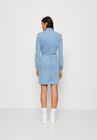 Ljusblå denimklänning med lång ärm, figursydd midja och knälång nederdel, med en enkel skärning och sömnadsdetaljer.