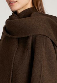 Abrigo de lana marrón con un diseño en capas y envolvente, con una textura suave y detalles de costura visibles a lo largo de los bordes.
