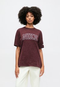 Kārtes krāsas t-krekls ar kontrastējošu "NIKE" logotipu. Īsas piedurknes un apaļa apkakle, izgatavots no teksturēta auduma.