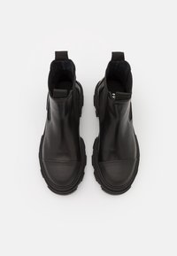 Černé kožené kotníkové boty s elastickými bočními panely, zaoblenými špičkami a texturovanými gumovými podrážkami. Obsahují dvě poutka na horních okrajích.