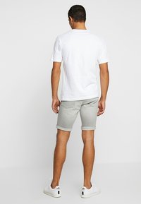 Bílá tričko, šedé denimové šortky, ohrnuté manžety, lehká tkanina. Bílé tenisky s černým akcentem. Model stojící, pohled zezadu.