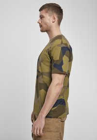 Olive zöld t-shirt sötétkék és bézs árnyalatú geometriai mintával. Rövid ujjú és kerek nyakú dizájn. Simas textúra.