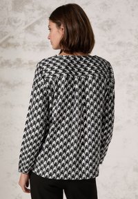 Svartvitt houndstooth-mönstrad blus med långa ärmar, rundad halsringning och lös passform, med en veck bak.