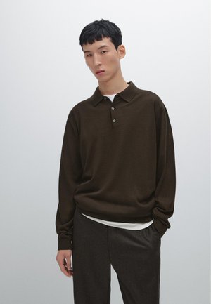 Brown long-sleeve polo shirt with a collar, featuring a relaxed fit and three buttons. Layered over a white shirt, paired with dark trousers.