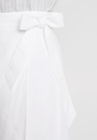 Vit linneomslagkjol med en knuten rosett i midjan. Tyget har en mjuk textur och designen är enkel och elegant.