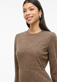 Robe marron à manches longues côtelées avec un col rond, un tissu texturé et une silhouette ajustée. Présente des détails de couture subtils.